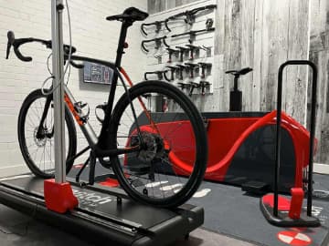 side view of setup system with bike loaded, smart bike behind it, and the demo saddles and handlebars for the fitting process on the wall.